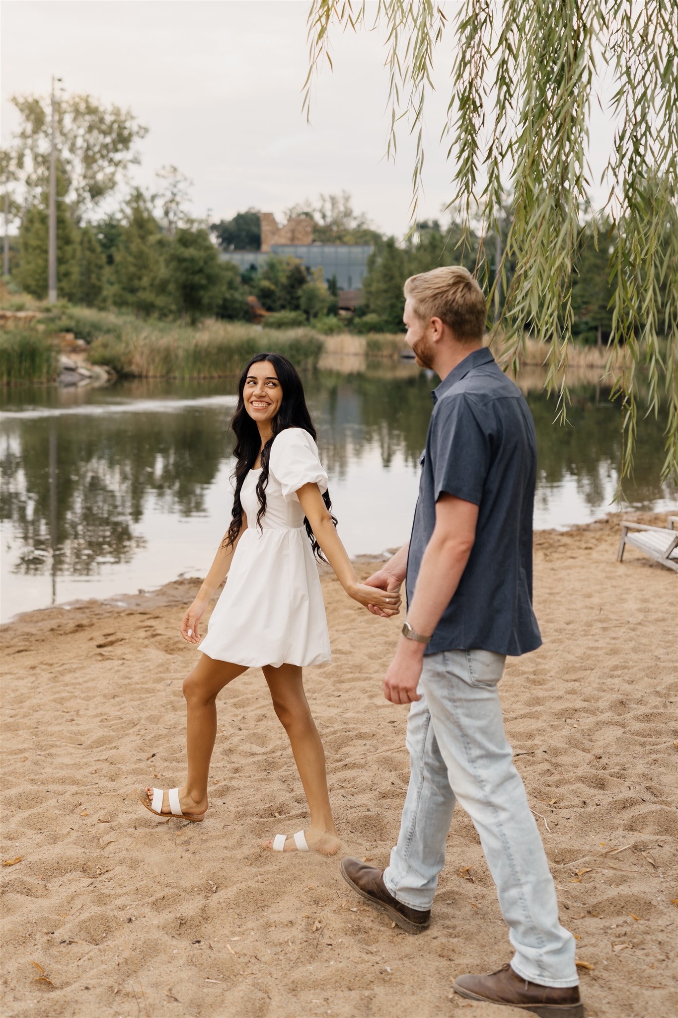 Couple holding hands beneath Willow Tree during romantic Tulsa engagement photos.