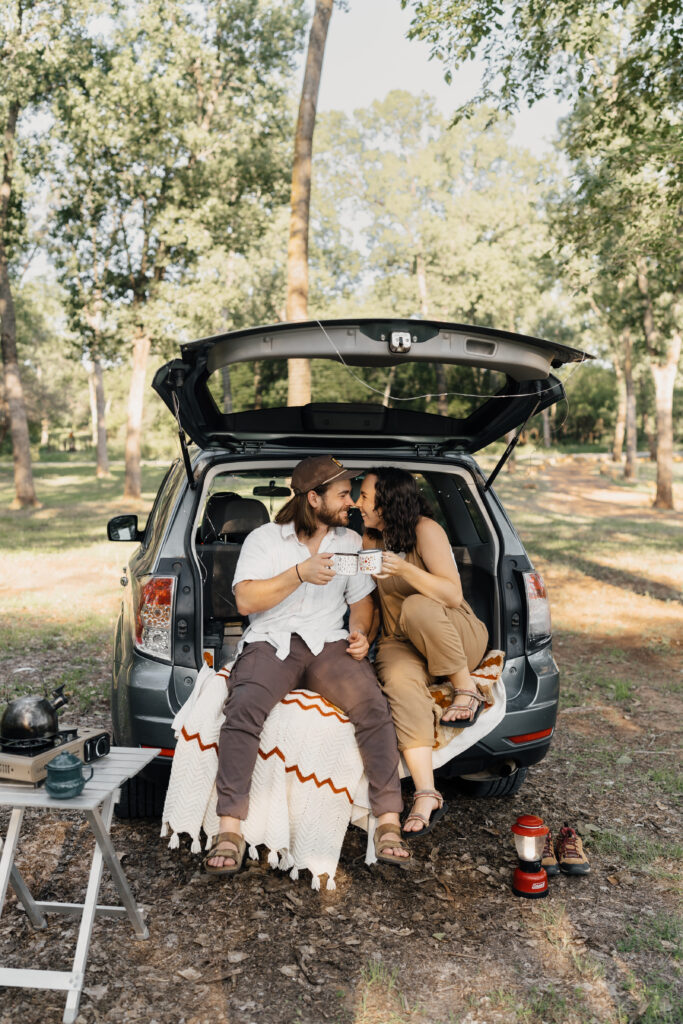 Engaged couple sharing coffee mugs during a cozy camping-inspired engagement session in Oklahoma