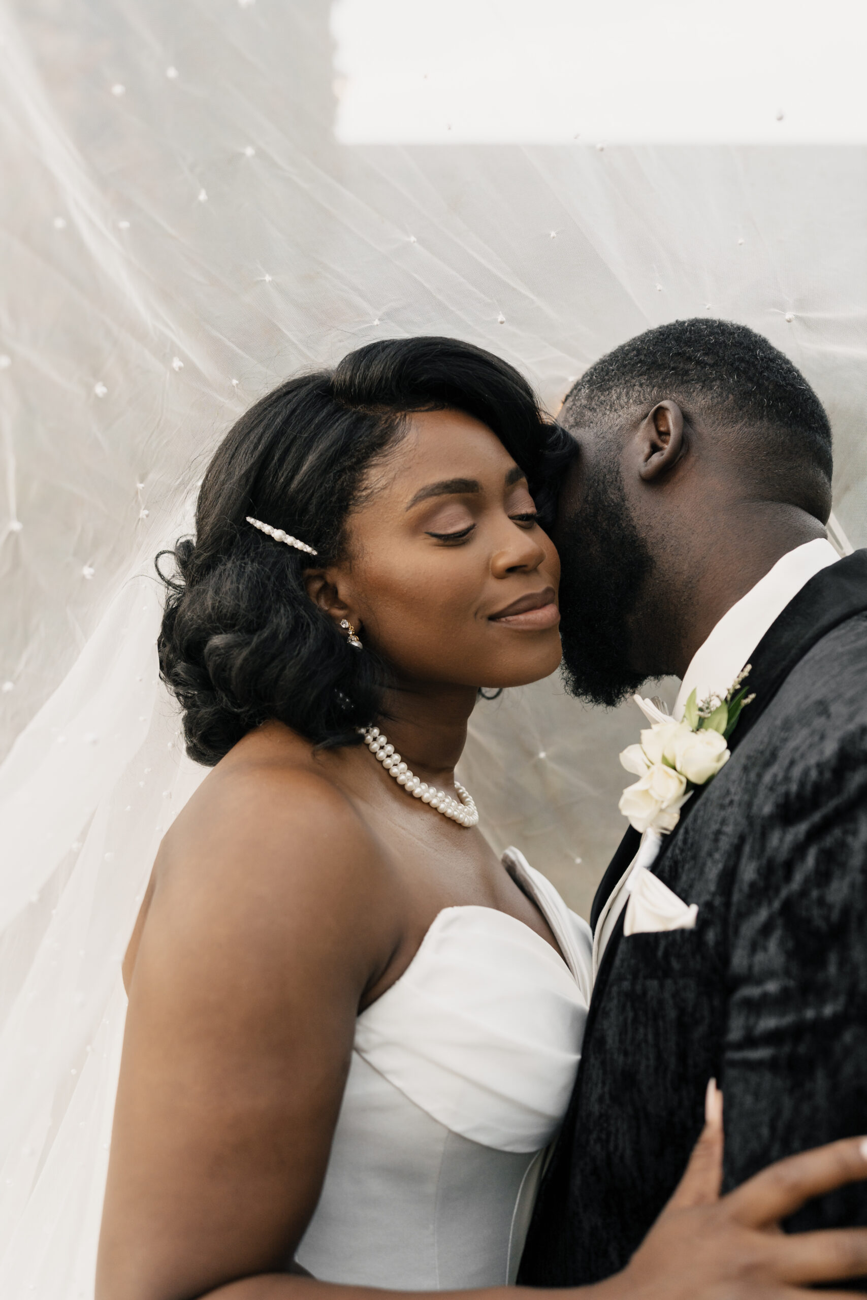 Groom in linen suit kissing bride on cobblestone path
