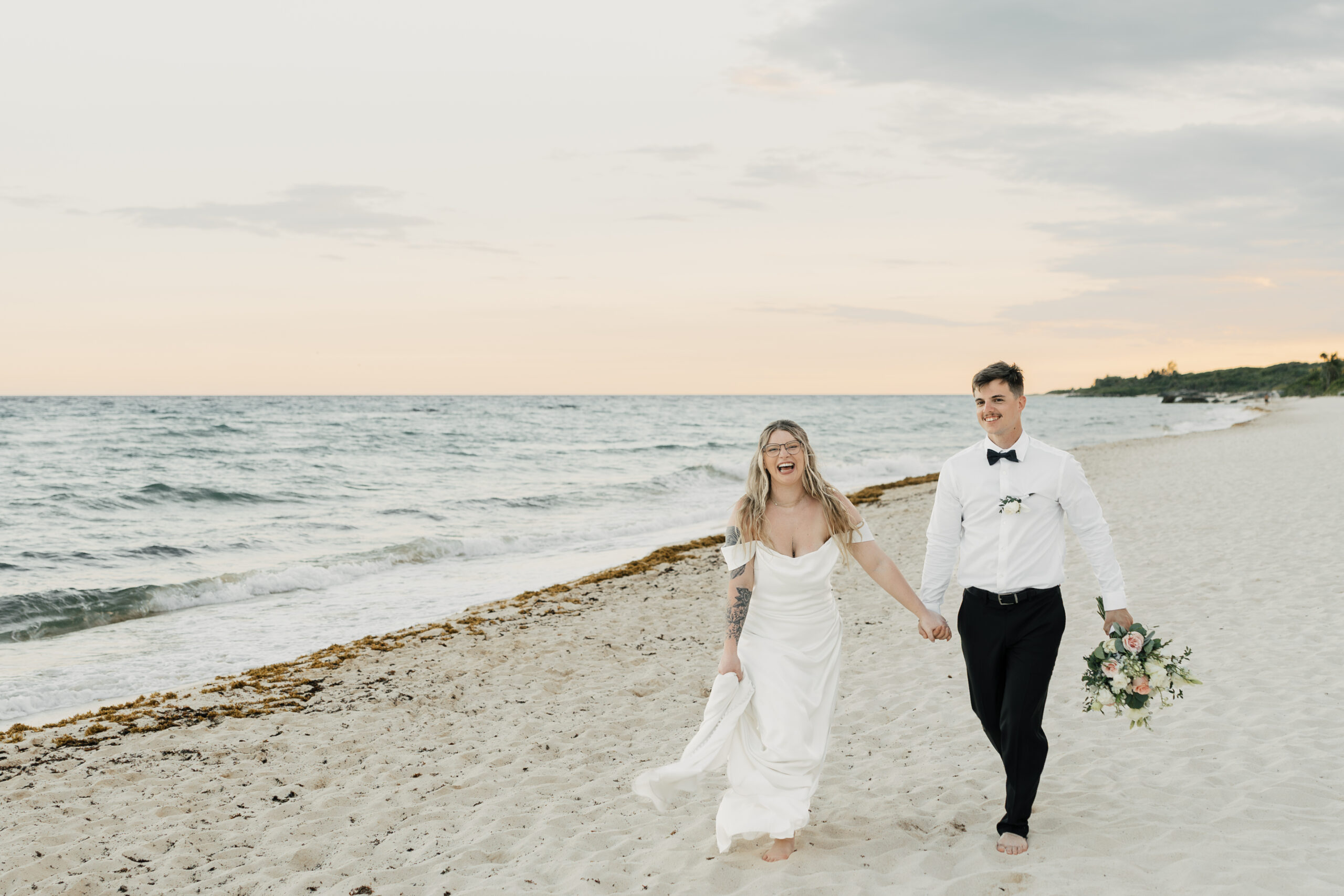 Bride and groom walking along shoreline at sunset